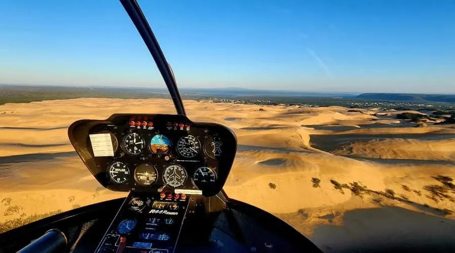 Helicopter cockpit view over sand dunes and coastal landscape