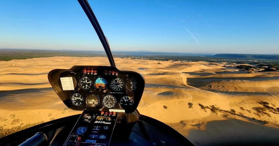Helicopter cockpit view over sand dunes and coastal landscape